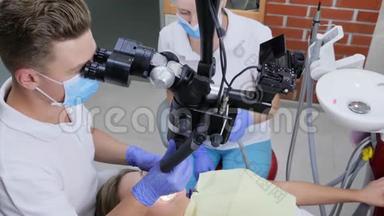 牙科医生在病人口腔内通过<strong>光学显微镜</strong>观察`助手帮助附近的医院
